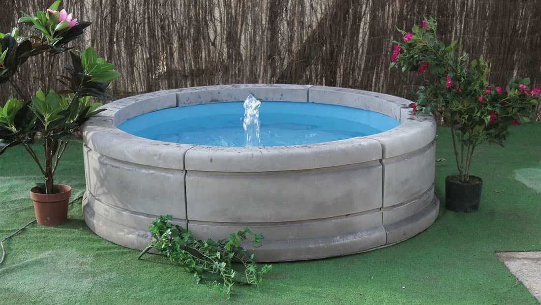 A round cast stone pool surround with a small fountain jet