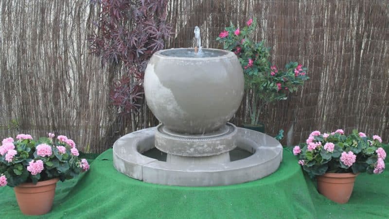 A spherical stone fountain on a decorative stone surround
