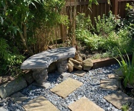 Small curved stone bench in a gravel garden with stepping stones