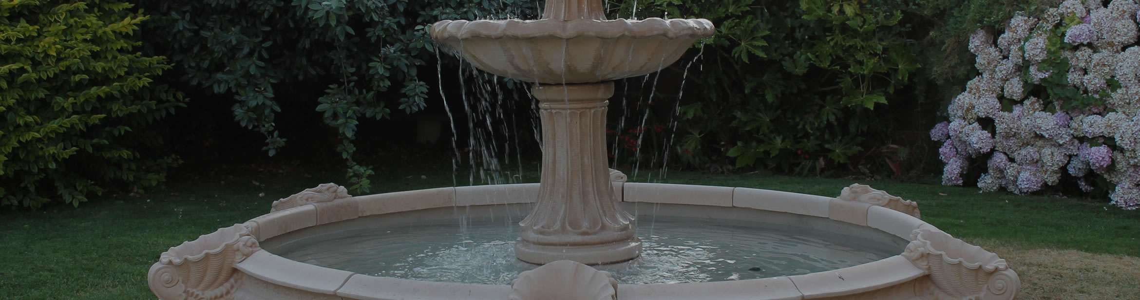 Tiered stone fountain in a landscaped garden, shown in proportion to the surrounding lawn and planting